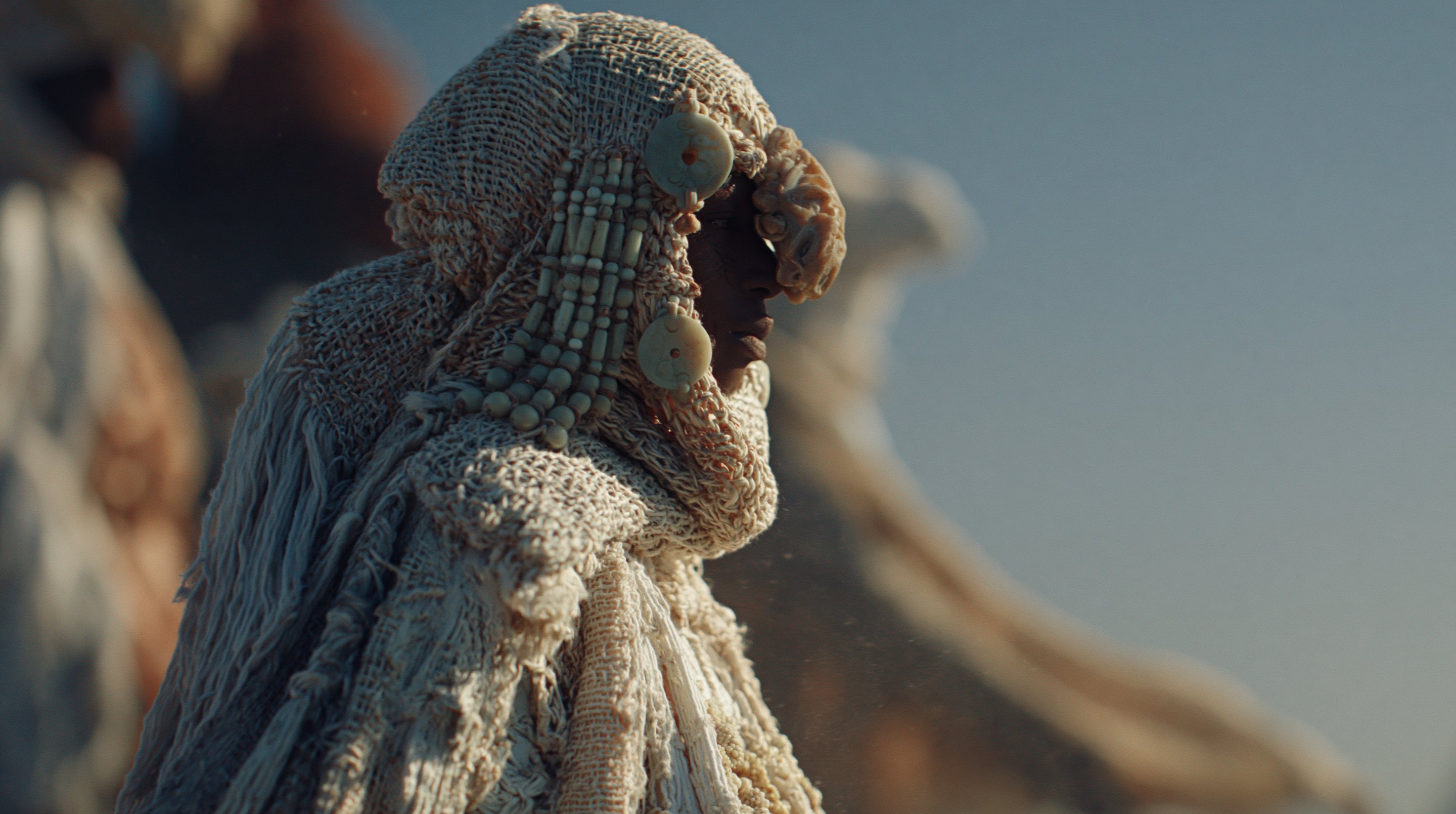 Close view of layered ceremonial textiles, carved ornaments and beadwork catching warm sunlight.
