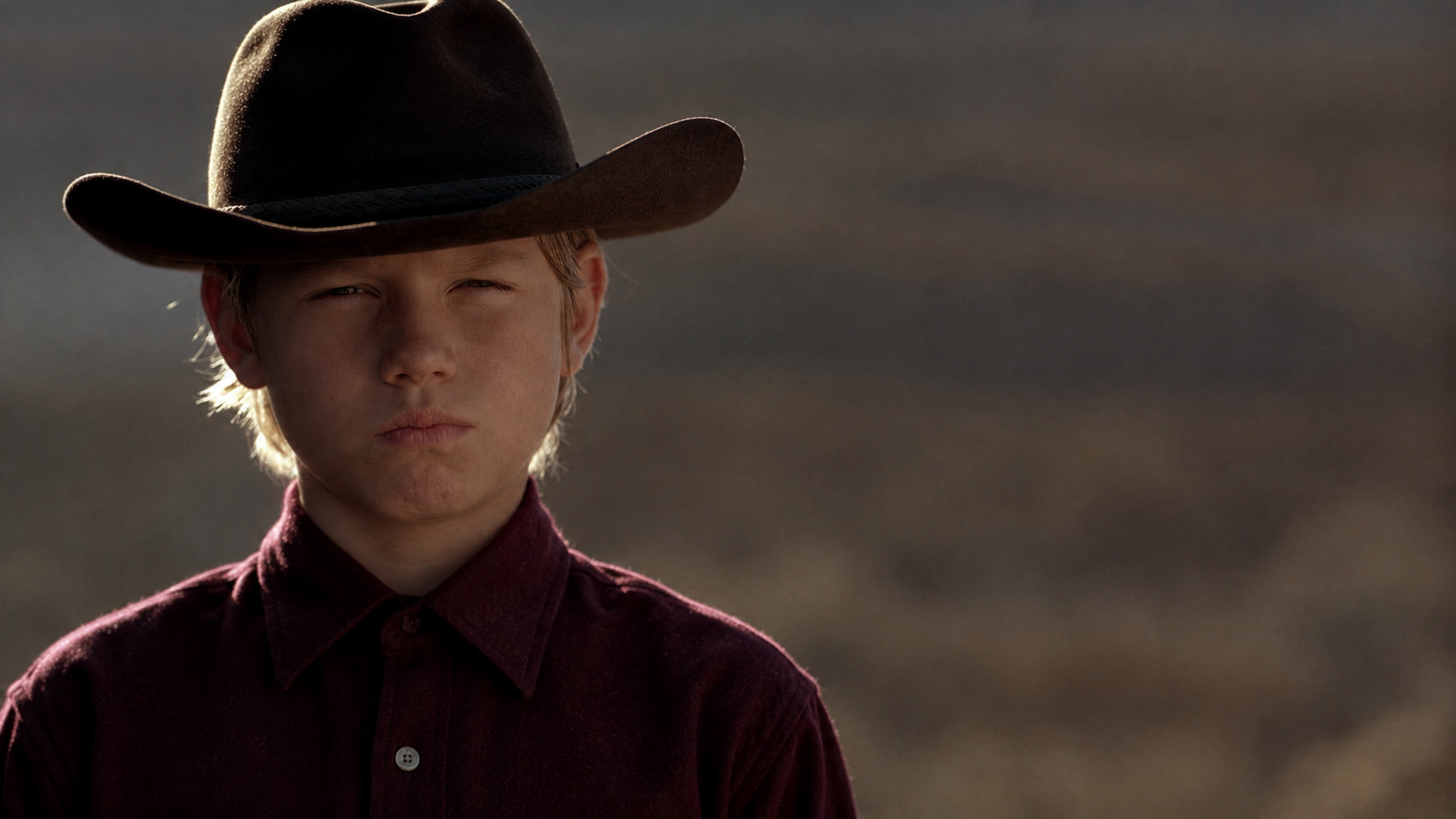 Close-up of a boy in a black cowboy hat and dark red shirt, staring down his opponent.